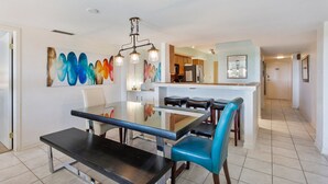 A modern kitchen with a central island, a dining area with a glass table, and a hallway leading to a door.