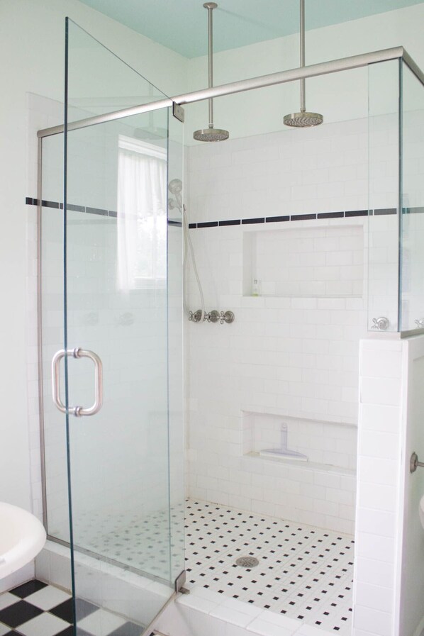 Ducha con cerramiento de vidrio, suelo de baldosas blancas y puerta de cristal con manija.