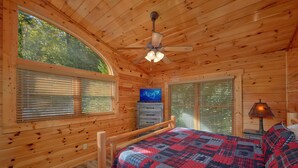 A wooden cabin bedroom with a bed, a ceiling fan, a dresser, and a television. - Natural Attractions: Theater, Gameroom, Hot Tub (Gatlinburg)