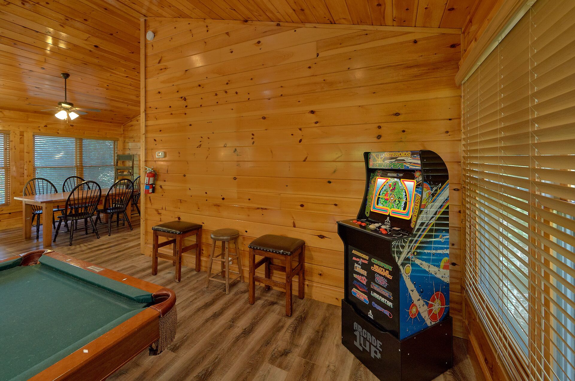Una cabaña de madera con mesa de billar, comedor y máquina de videojuegos.