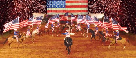 A performance with riders on horses, surrounded by American flags and fireworks.