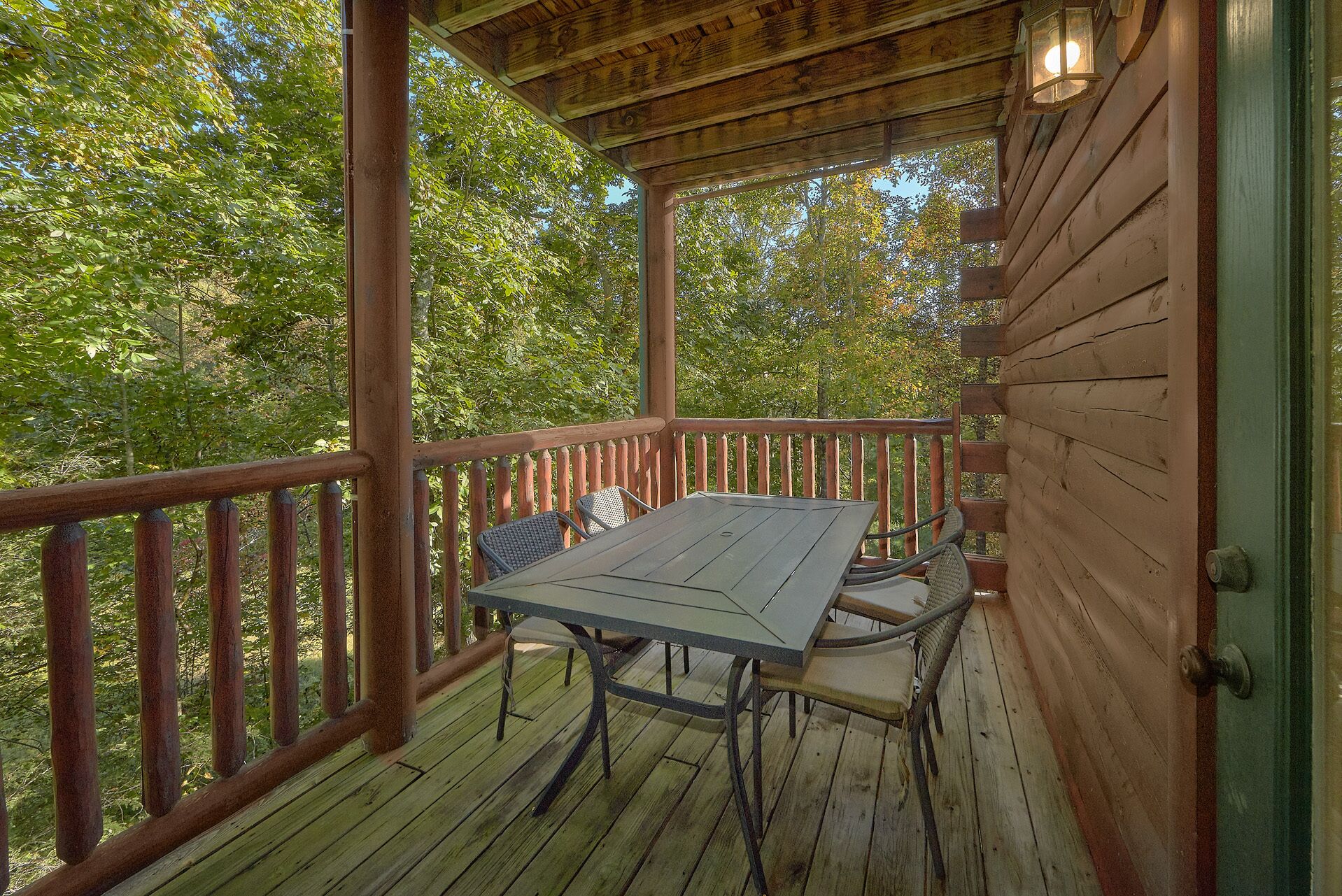 Une terrasse en bois, agrémentée d’une table et de chaises, entourée d’une balustrade en bois, et offrant une vue sur une zone boisée.