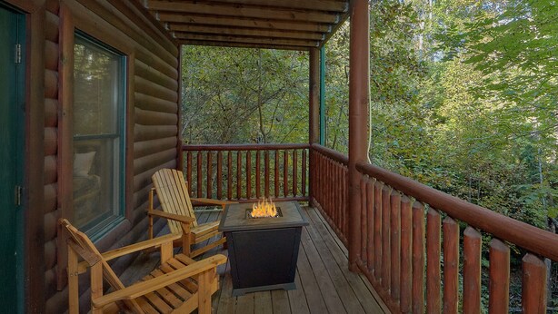 A wooden deck with a fire pit, a wooden chair, and a window overlooking a forested area. - Natural Attractions: Theater, Gameroom, Hot Tub (Gatlinburg)