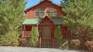 A log cabin with a green roof, a front porch, and a stone foundation. - Natural Attractions: Theater, Gameroom, Hot Tub (Gatlinburg)