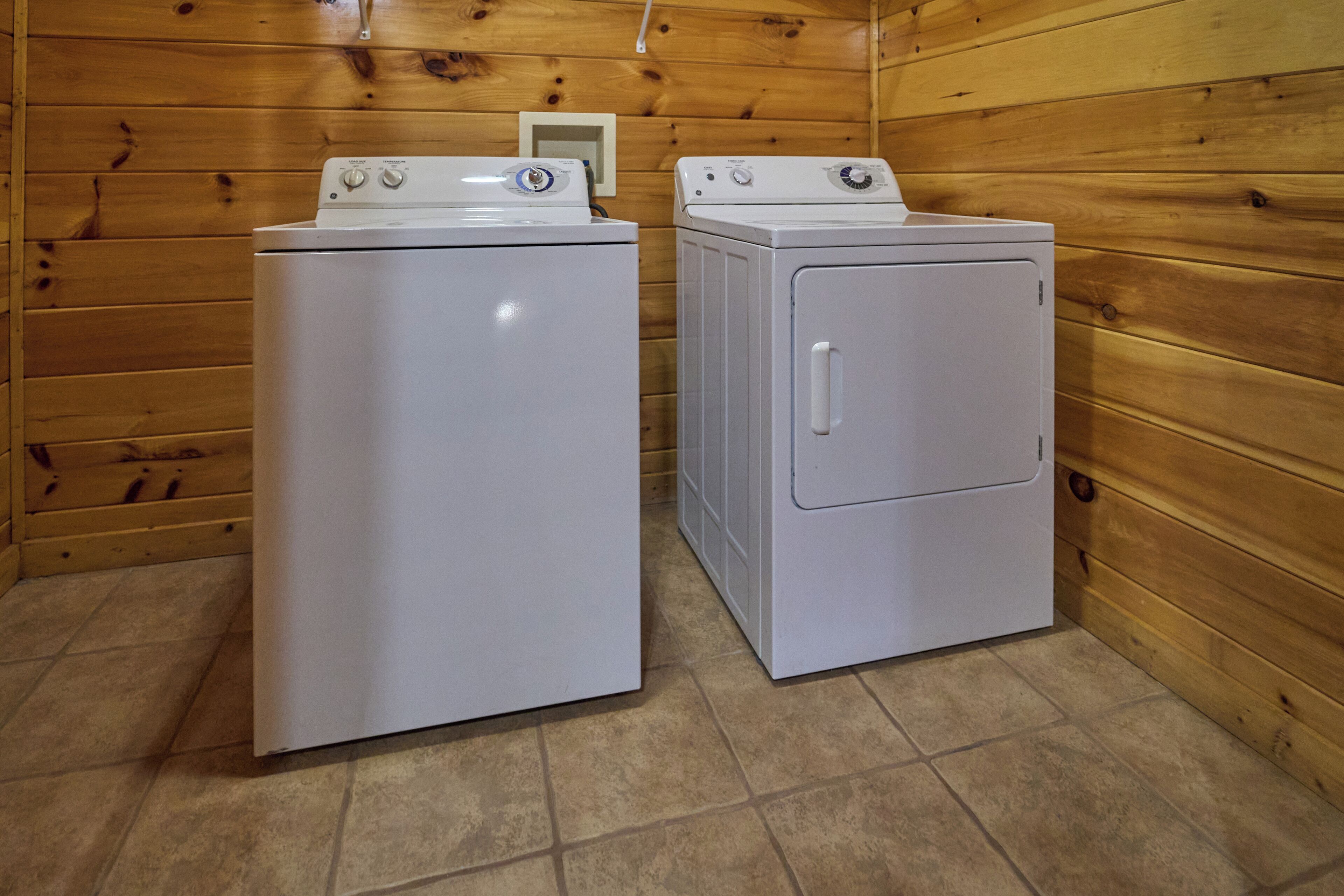 Two white washing machines in a wooden room with tiled flooring.