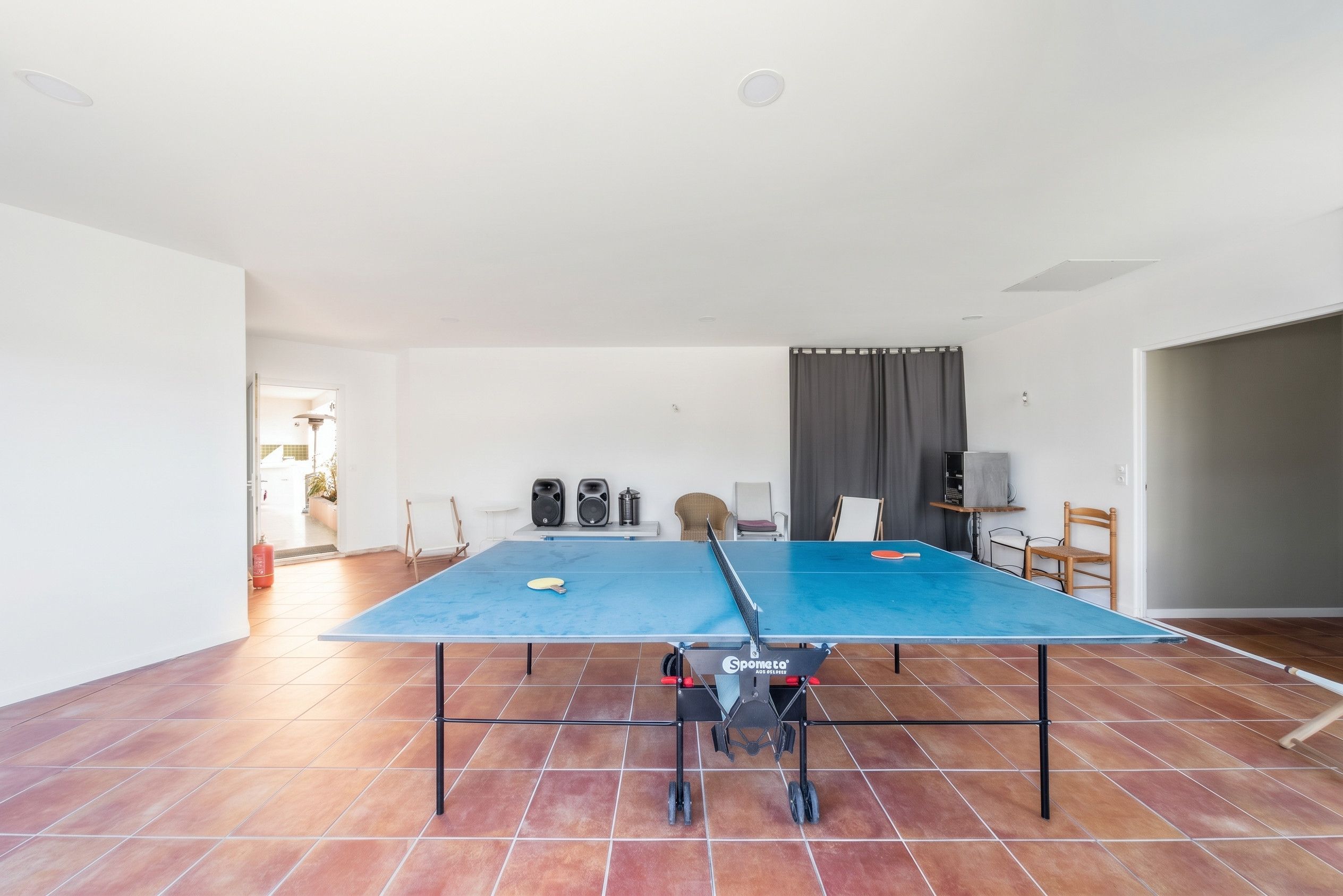 Una habitación amplia con mesa de ping pong, dos altavoces y extintor.
