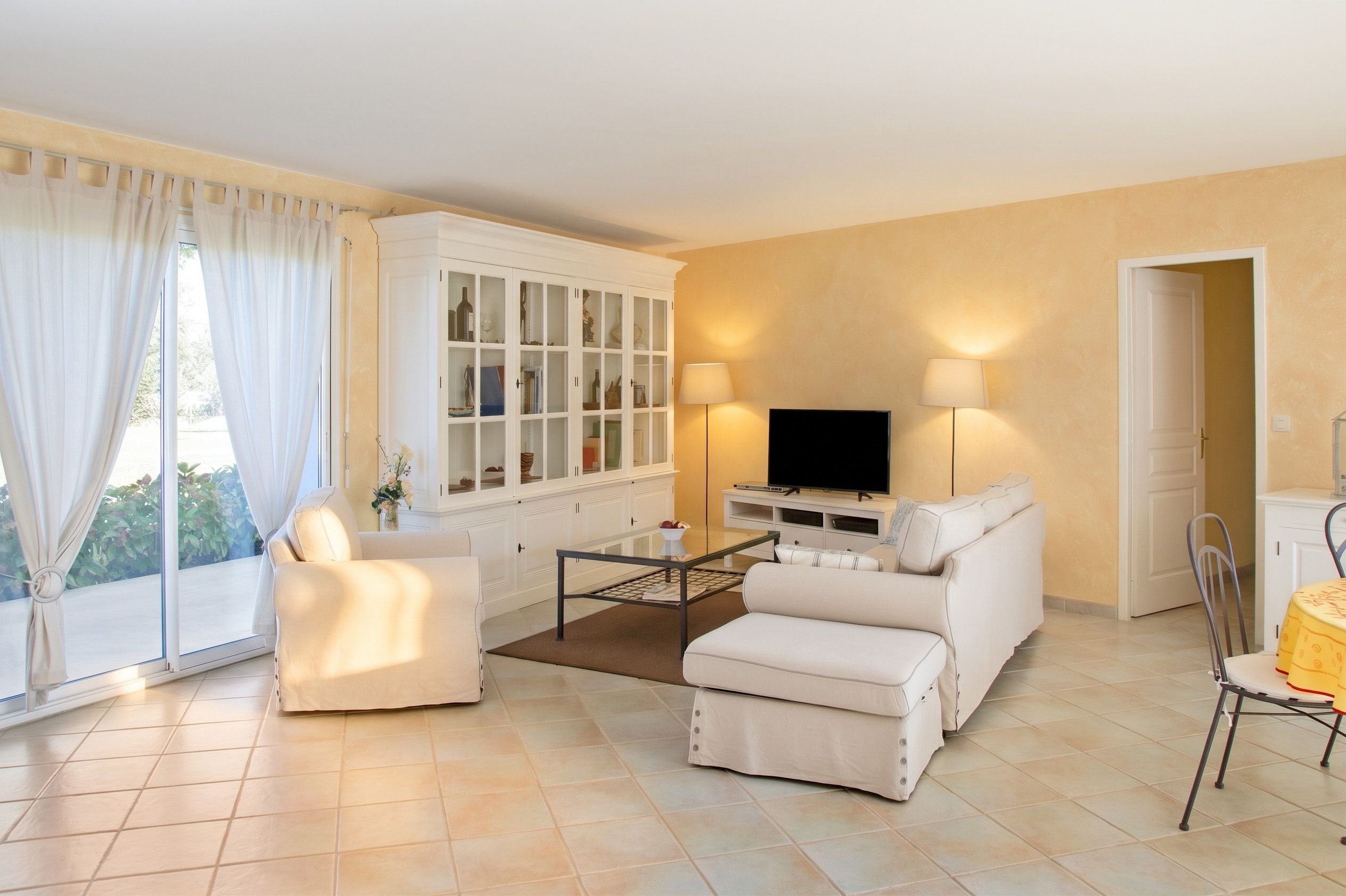 Ein Wohnzimmer mit einer Couch, Sesseln, Fernseher und einer Vitrine.
