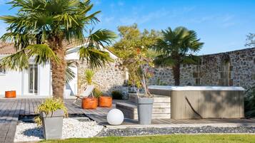 Un espace extérieur moderne, aménagé en terrasse, avec un mur en pierre, des palmiers et un jacuzzi.