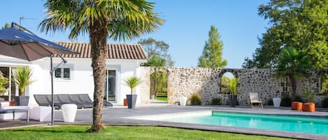 Una casa moderna con piscina, mobiliario exterior y un muro de piedra.