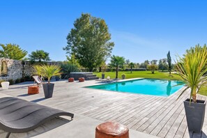 Una terraza de madera con piscina, sillas de descanso y plantas en macetas.