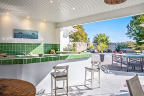 Una cocina moderna con salpicadero de azulejos verdes, una barra con taburetes y vistas a una piscina y jardín.