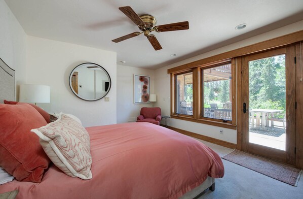 Une chambre dotée d’un grand lit, d’un ventilateur de plafond, d’une fenêtre donnant sur l’extérieur et d’une porte menant à un balcon.
