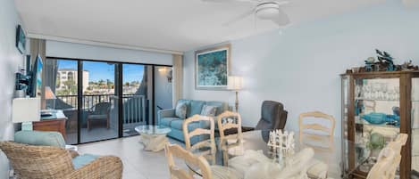 Un salon spacieux avec un balcon, un ventilateur de plafond, une table à manger avec des chaises et une vitrine contenant des objets décoratifs.