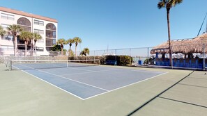 An outdoor tennis court with a net, surrounded by a fence, palm trees, and a building with arched windows. - Renovated 2 Story 2 bed 2 bath Cabana Unit w/ On-Site Dolphin Tiki! (Marco Island)