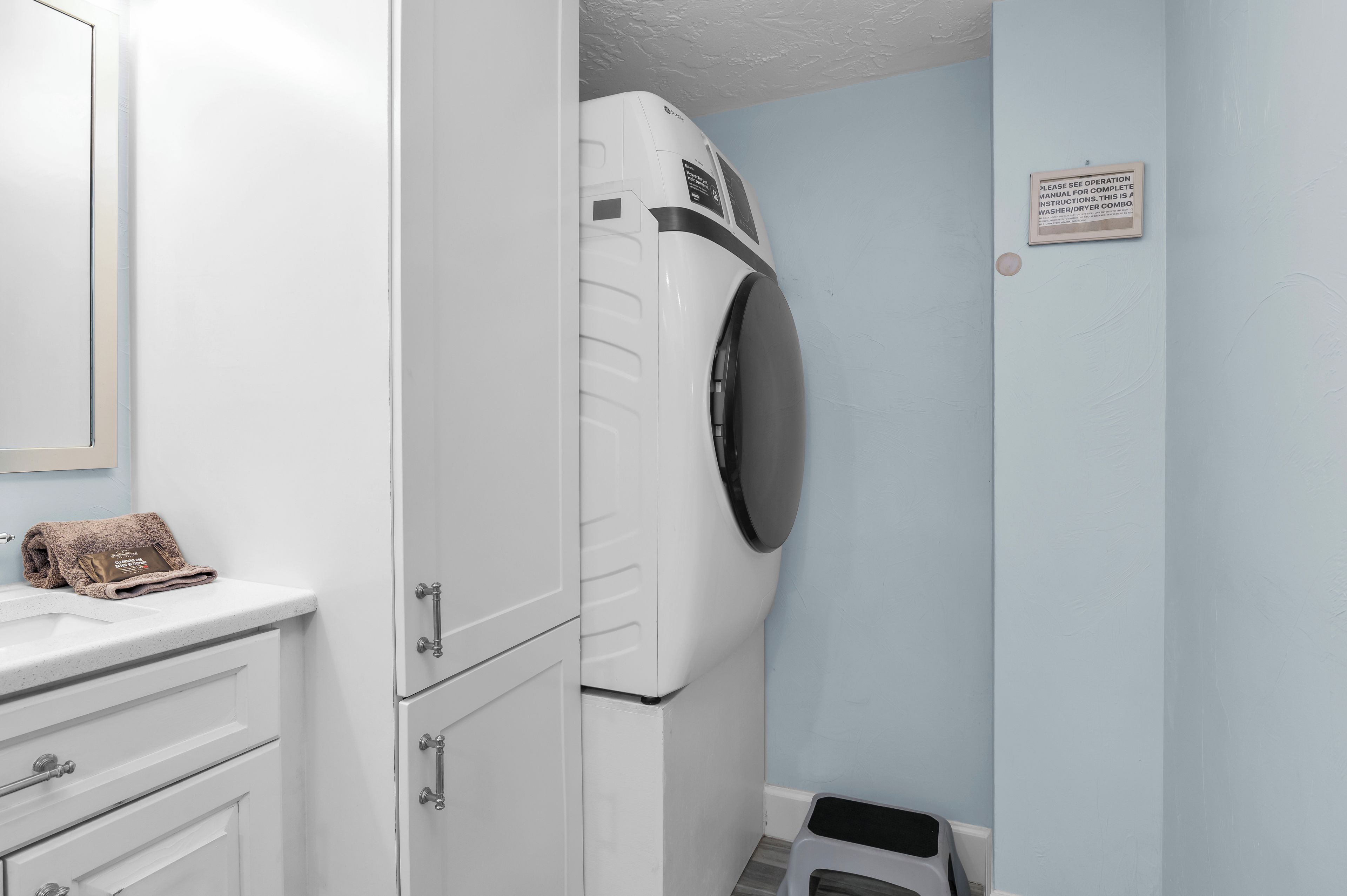 A compact laundry room with a front-loading washer and dryer, a small trash bin, and a towel on the counter.