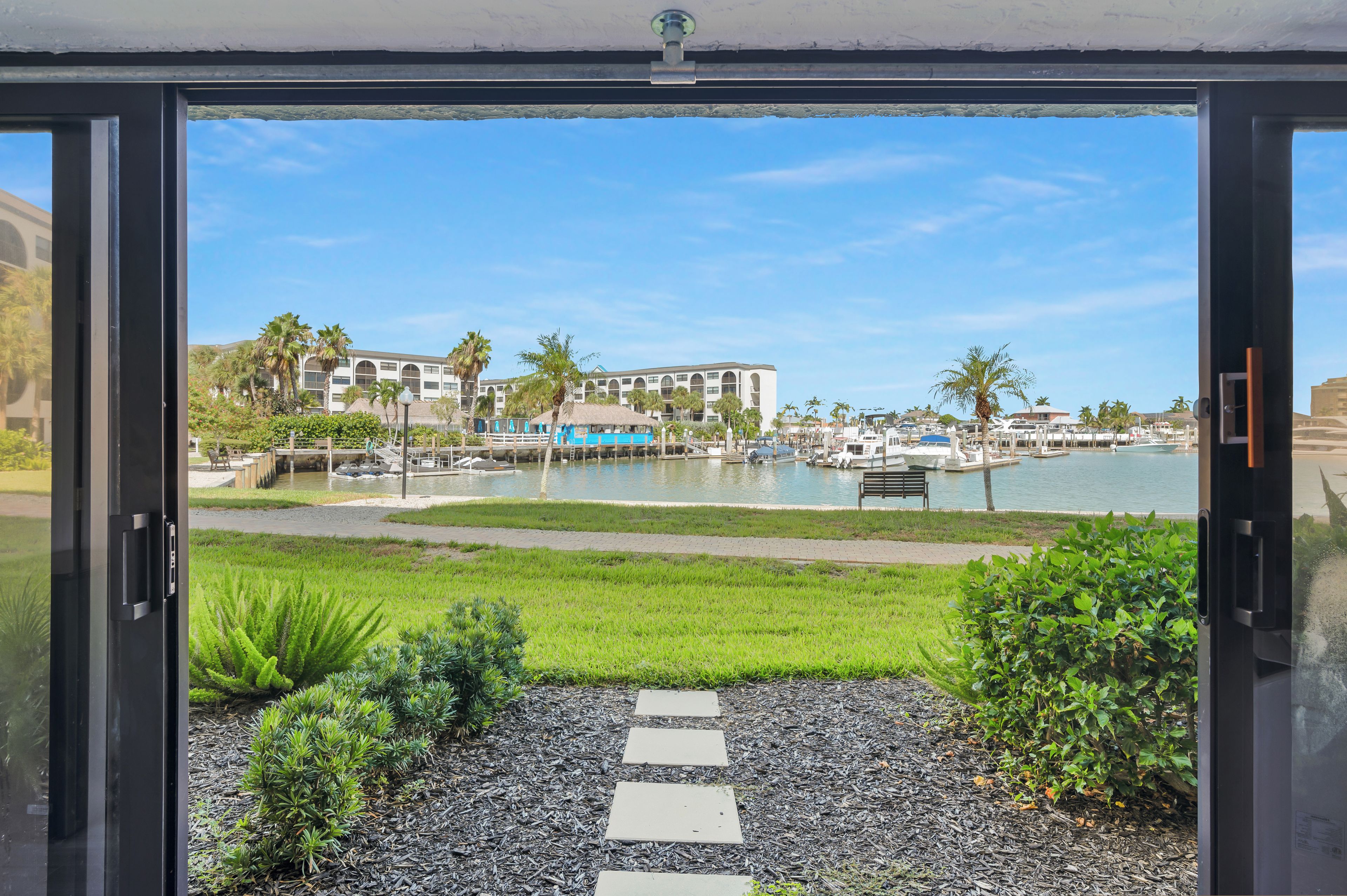 A view from a window overlooking a marina with boats, a pool, and a building with arched windows.