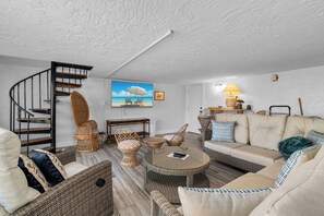 A living room with a spiral staircase, wicker furniture, a sofa, and a painting of a beach scene.