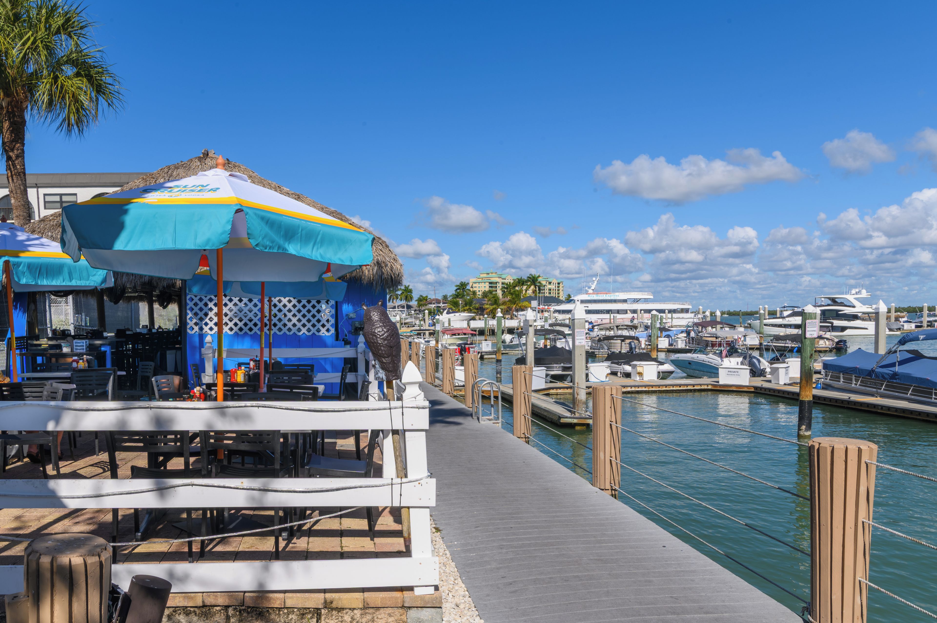 Ein Yachthafen mit vor Anker liegenden Booten, ein Restaurant mit Terrassenbereich und ein klarer, blauer Himmel.