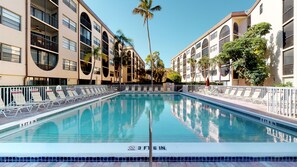 A swimming pool with a 3 ft 6 in depth, surrounded by a white fence, and adjacent to a multi-story building with balconies and palm trees. - Renovated 2 Story 2 bed 2 bath Cabana Unit w/ On-Site Dolphin Tiki! (Marco Island)
