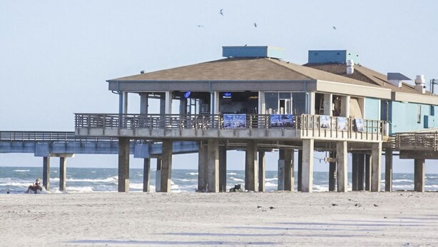 A beachside pier with a building that has a balcony and a view of the ocean.