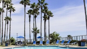 A swimming pool with blue lounge chairs and palm trees in the background.