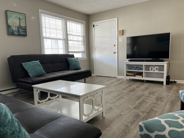 A living room with a black leather sofa, a white coffee table, and a television on a white stand. - Spacious & Close to Beach- Condo E (Ocean City)