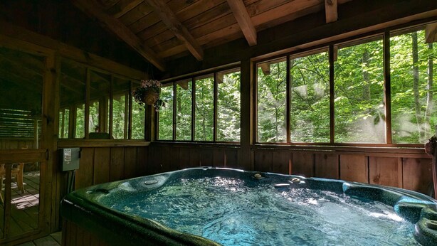 Ein Whirlpool in einer Holzhütte mit großen Fenstern mit Blick auf einen Wald.