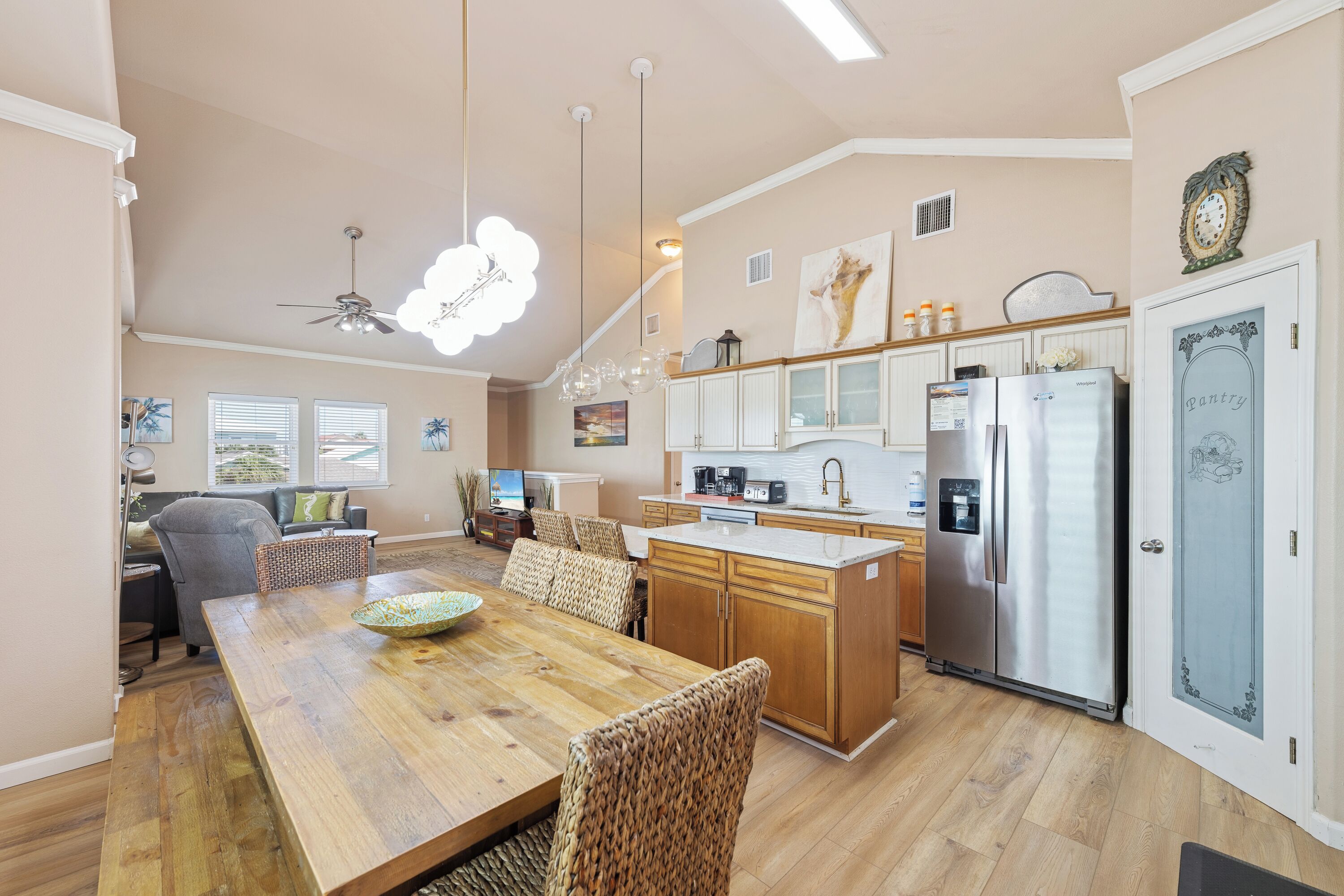 Een ruime keuken met houten kastjes, een koelkast van roestvrij staal en een eethoek met een houten tafel en geweven stoelen.
