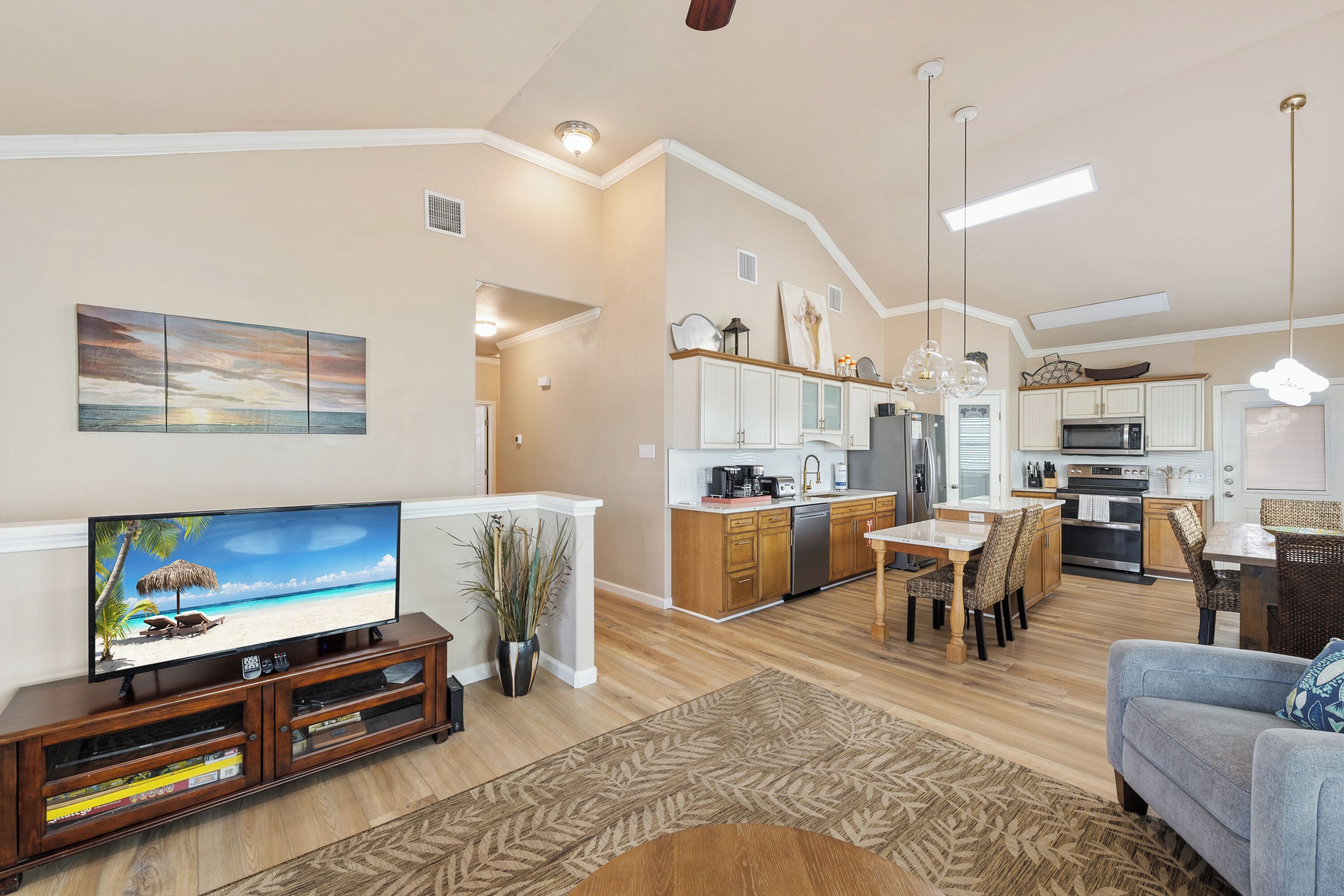 A modern kitchen with a dining area, a living room with a TV, and a hallway leading to another room.