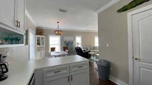 A spacious kitchen with white cabinetry, a dining area with a table and chairs, and a living room with a sofa and a coffee table. - Luxury Condo Boasting Lagoon Oasis Pool Near White Sandy Beaches (Pensacola)