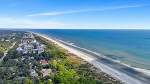 An aerial view of a coastal area with a beachfront hotel complex, dense greenery, and a clear blue sky. - 17 Firethorn - HGTV "Wow-Worthy", Pool, Fire Pit (Hilton Head Island)