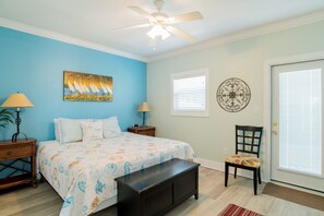 Un dormitorio con cama, mesita de noche, silla, banco, ventilador de techo, ventana con persianas y puerta.