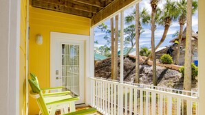 Un bâtiment jaune avec une porte blanche et un porche doté de chaises vertes.