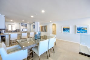 A modern kitchen with white cabinetry, a glass dining table, and a seating area with white chairs.