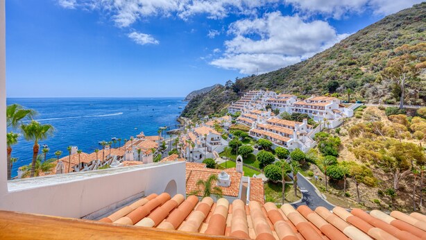 Eine Küstenstadt mit terrakottafarbenen Dächern, blauem Himmel und Blick auf das Meer.