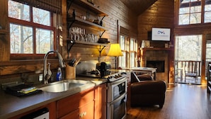 Ein rustikales Cabin-Interieur mit einer Küche, die ein Spülbecken, einen Herd und einen Backofen umfasst, einem Essbereich mit Tisch und Stühlen sowie einem Kamin.
