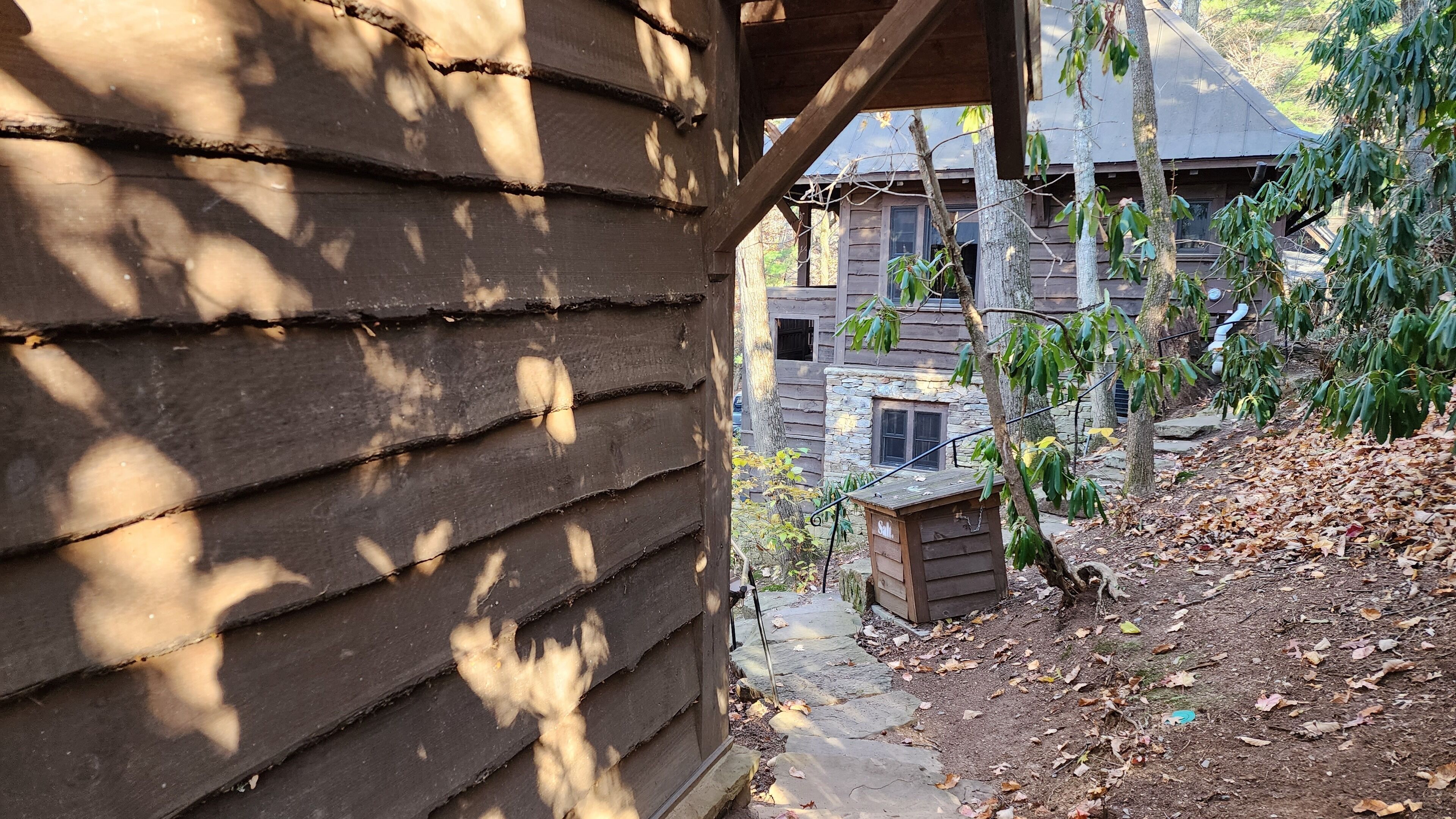 A wooden cabin with a stone foundation, surrounded by trees and a stone pathway.
