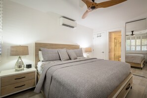Un dormitorio moderno con una cama grande, lámparas de noche, ventilador de techo y vestidor.