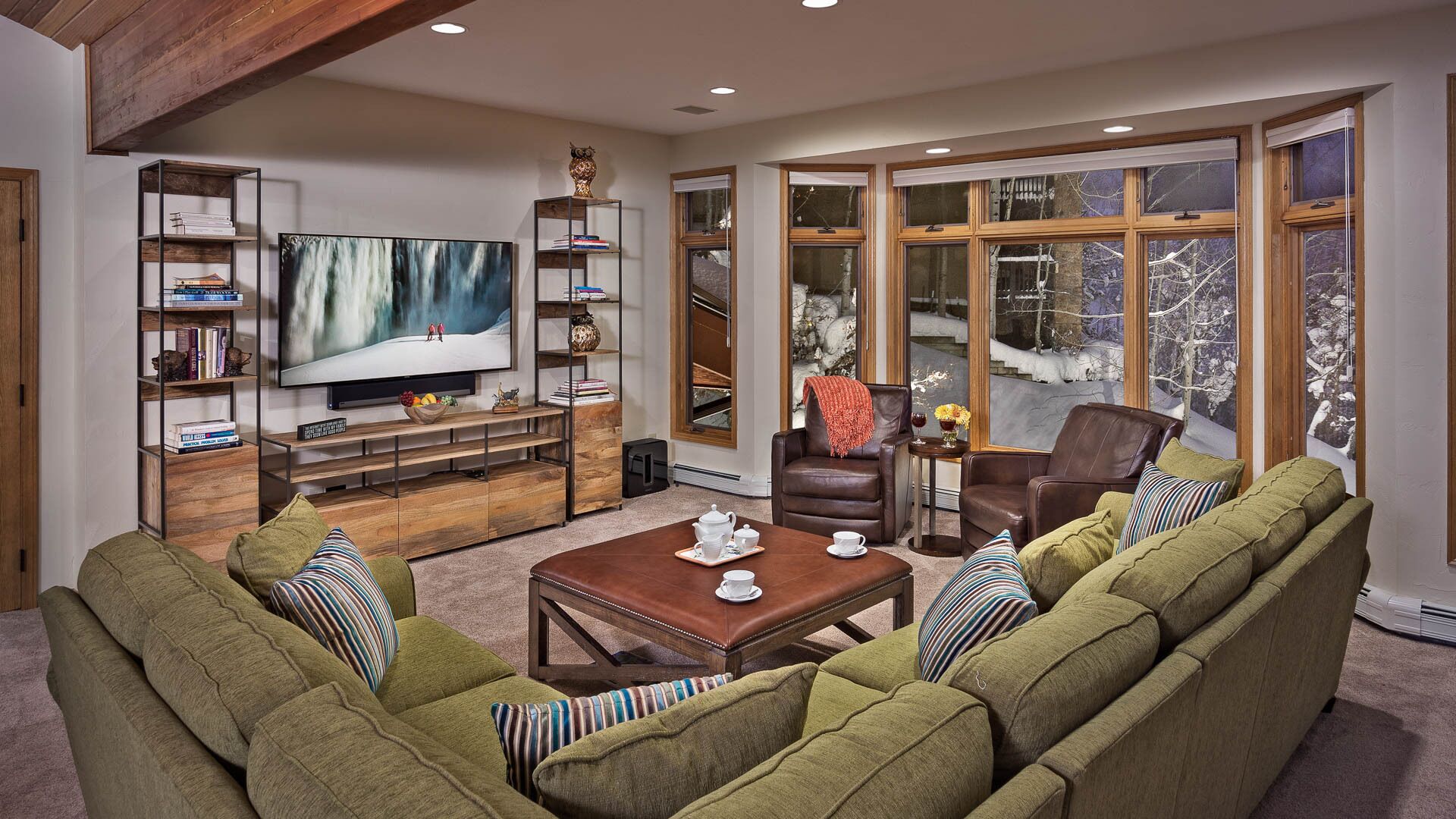 A cozy living room with a large flat-screen TV, comfortable seating, and a bookshelf.