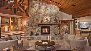 Un espacio habitable amplio con chimenea de piedra, asientos cómodos y un televisor al fondo.