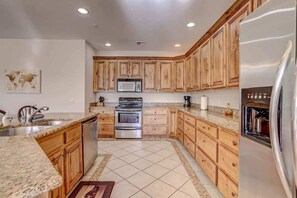 A kitchen with wooden cabinets, a stainless steel refrigerator, a microwave, and a stove. - Las Palmas Resort #1708 | All-Inclusive Amenities (Saint George)