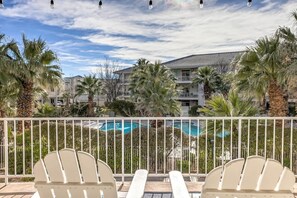 A balcony with white chairs, a pool, and a building with balconies in the background. - Las Palmas Resort #1708 | All-Inclusive Amenities (Saint George)