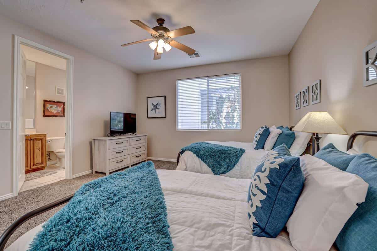 Ein Schlafzimmer mit zwei Betten, einem Deckenventilator, einem Fernseher und einem Fenster mit Jalousien.