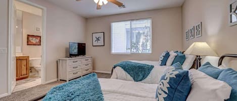 Een slaapkamer met twee bedden, een plafondventilator, een televisie en een raam met jaloezieën.