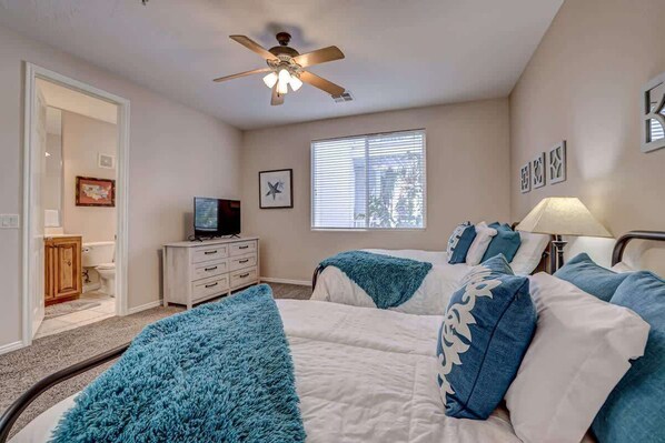 A bedroom with two beds, a ceiling fan, a television, and a window with blinds. - Las Palmas Resort #1708 | All-Inclusive Amenities (Saint George)