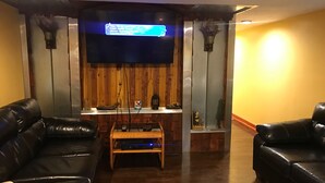 Una sala de estar con una pared de madera, un televisor de pantalla plana montado sobre una repisa de madera y dos sofás de cuero negro.