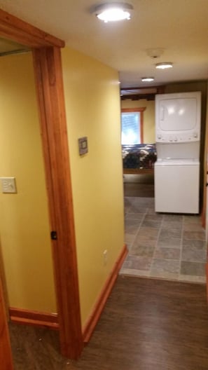 Un couloir aux murs jaunes, une porte en bois et, au fond, un appareil électroménager blanc.