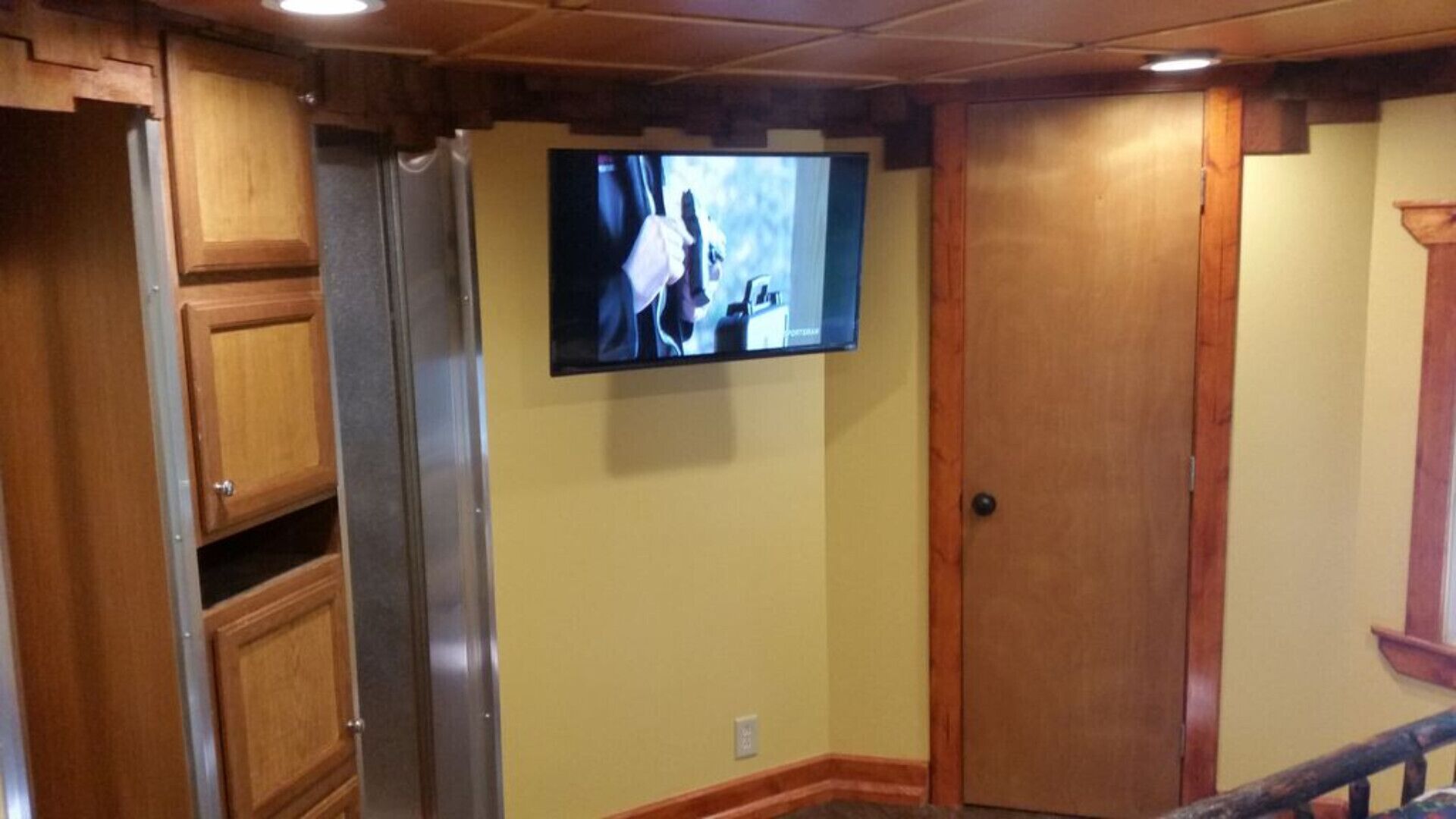 Una cocina con armarios de madera, un refrigerador de acero inoxidable y un televisor montado en la pared.