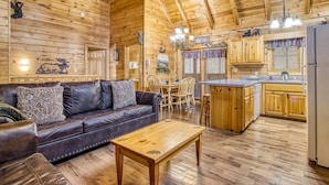 Un interior de cabaña acogedor con una zona de comedor de madera, un sofá de cuero y una cocina con armarios de madera y un refrigerador.
