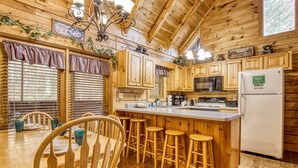 Cocina de cabaña de madera con comedor, taburetes de madera y un refrigerador.